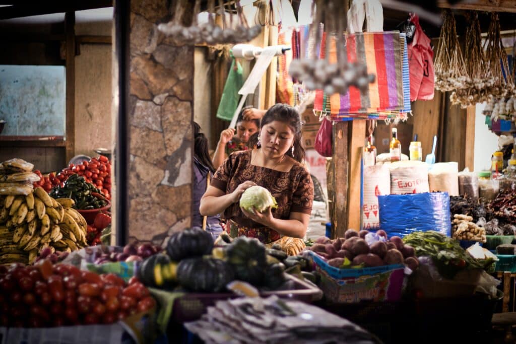 a woman is standing in a market selling fruit and vegetables