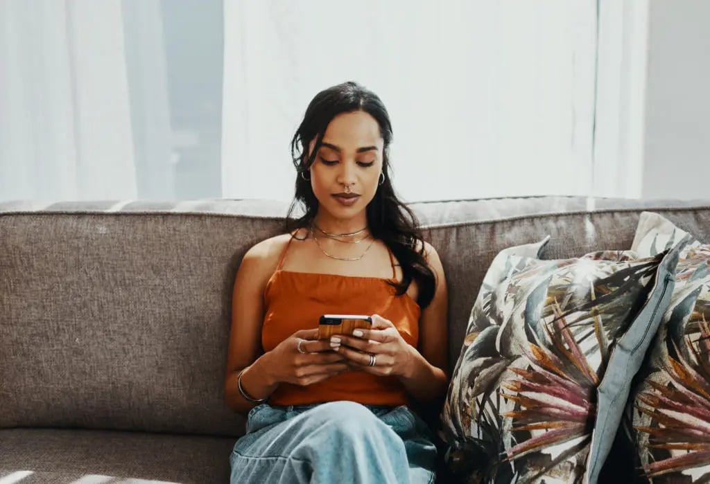 Beginner investing: woman sitting on a couch and using her phone