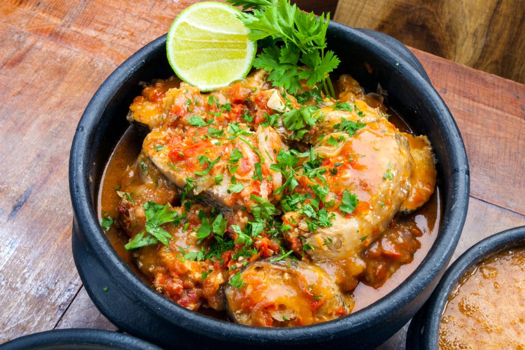 a bowl of chicken with sauce and lime on a wooden table