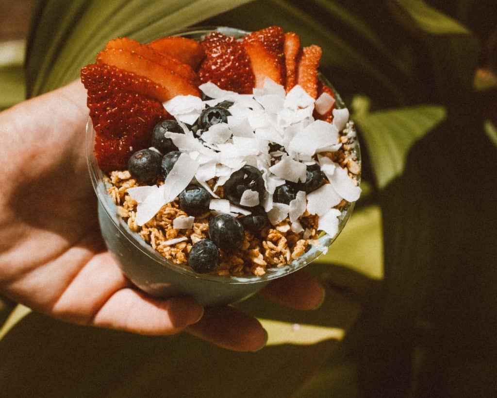 a person holding a bowl of granola with berries and coconut