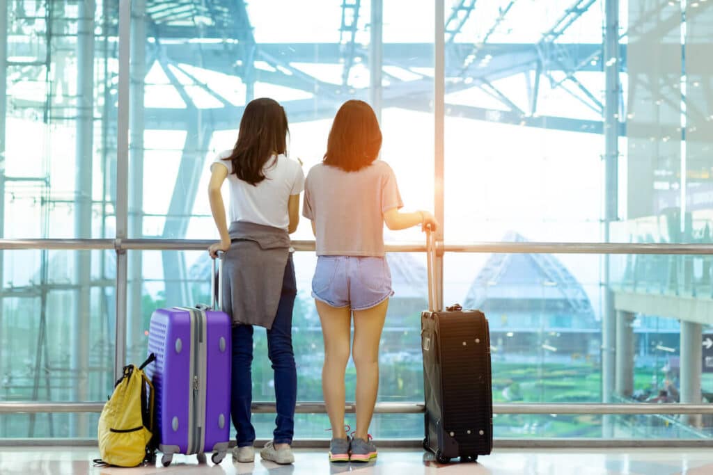 Two travelers holding their suitcases at an airport