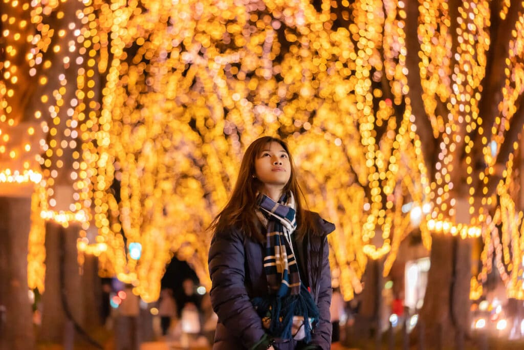 A woman looks up at trees covered in lights during Christmas in Japan