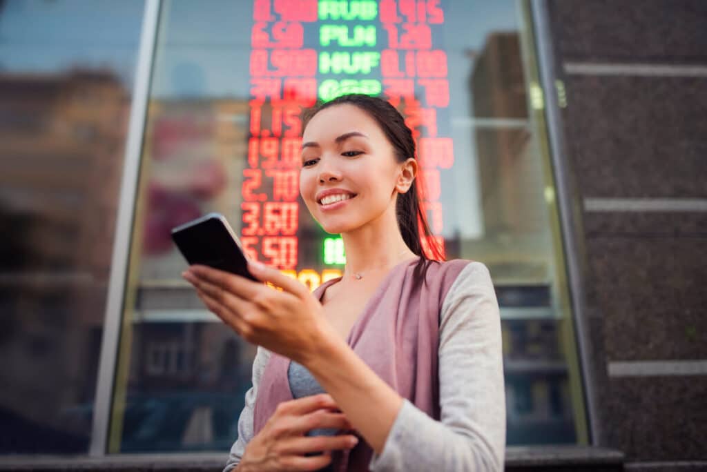 Where to exchange currency: A smiling woman looks at her phone outside of a currency exchange store