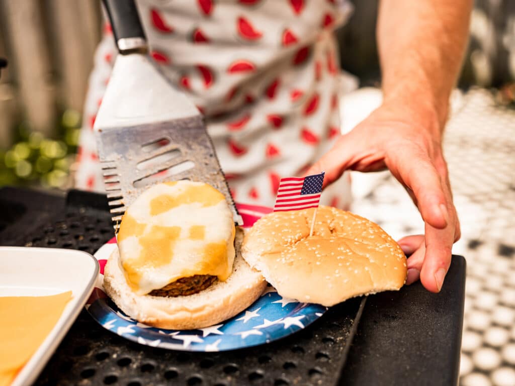 Hands of Chef setting up cheeseburger meal from BBQ grill lunch outdoor at 4th July backyard celebration.
