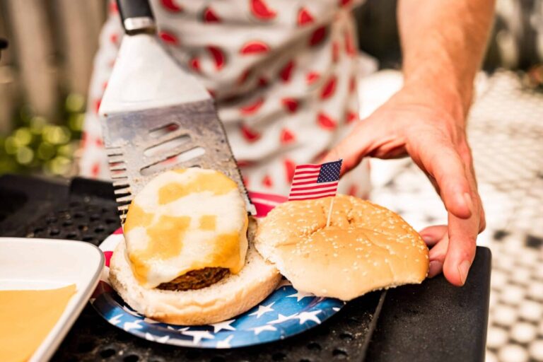 Hands of Chef setting up cheeseburger meal from BBQ grill lunch outdoor at 4th July backyard celebration.