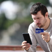 Worried man buying online with credit card and smart phone sitting in a rural town