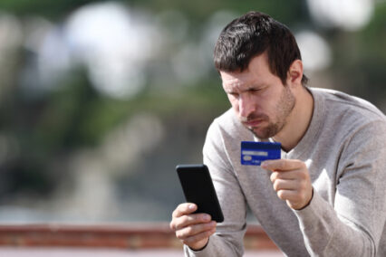 Worried man buying online with credit card and smart phone sitting in a rural town