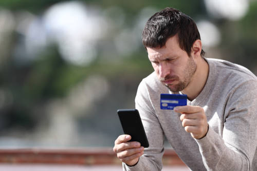 Worried man buying online with credit card and smart phone sitting in a rural town