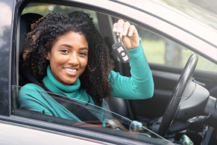 Woman holding up keys to her first new car.