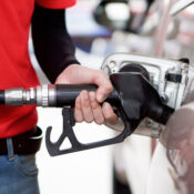 Gas station worker in red uniform filling up bronze pickup truck tank.