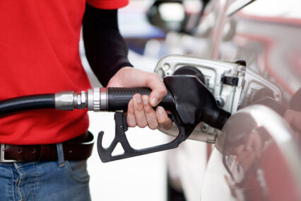 Gas station worker in red uniform filling up bronze pickup truck tank.