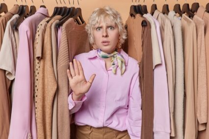A young woman makes stop gesture asks not to spend much money on clothes.