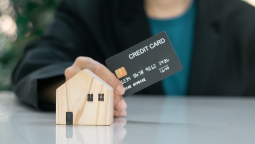 Man hold credit card with wooden model house.