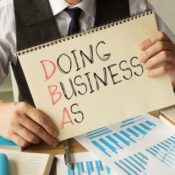 Doing business as DBA is shown on a note pad by a business person.