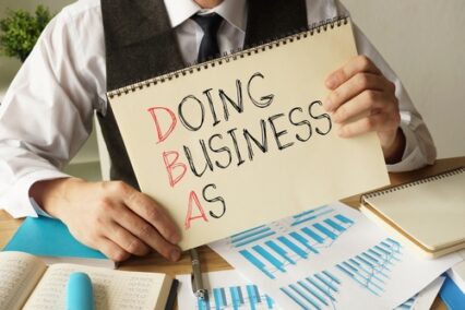 Doing business as DBA is shown on a note pad by a business person.