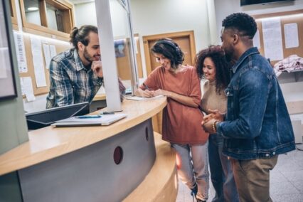 A group of students gathers around in the college lobby, each one diligently waiting on their college applications.