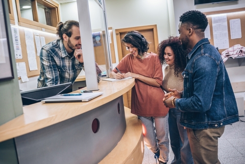A group of students gathers around in the college lobby, each one diligently waiting on their college applications.