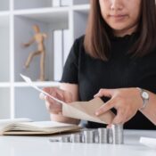 Young Woman Planning to Save Money by Counting Coins and Organizing Finances at Home Office Desk with Notebook and Envelopes
