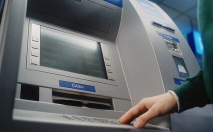 Unrecognizable person entering pin code on ATM keyboard to withdraw money.