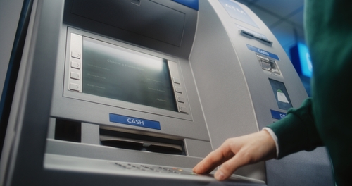 Unrecognizable person entering pin code on ATM keyboard to withdraw money.