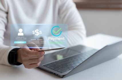 Close-up of hand holding credit card with virtual payment success interface on laptop representing secure online transaction and digital financial technology.