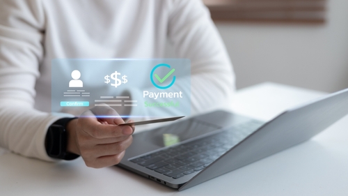 Close-up of hand holding credit card with virtual payment success interface on laptop representing secure online transaction and digital financial technology.