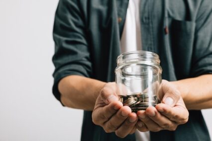 Hand of businessman holding a jar full of coins and the coins are in his palm
