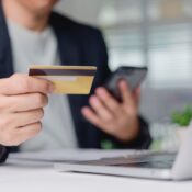 Customer confirming online purchase with credit card and smartphone on office desk near laptop