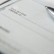 A black pen is on a blank check with its tip resting near the payment amount line, ready for someone to fill in the necessary details for a financial transaction.