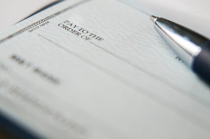 A black pen is on a blank check with its tip resting near the payment amount line, ready for someone to fill in the necessary details for a financial transaction.