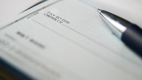 A black pen is on a blank check with its tip resting near the payment amount line, ready for someone to fill in the necessary details for a financial transaction.