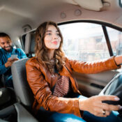 Taxi driver driving car with passenger sitting in background and using smart phone