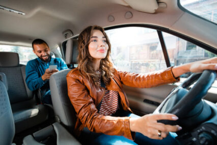 Taxi driver driving car with passenger sitting in background and using smart phone