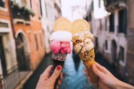 Beautiful and delicious Italian gelato in waffle cone in front of streets and bridges of Venice.