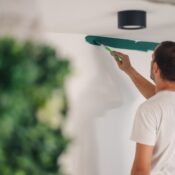 Professional house painter carefully applying green paint to a white wall, working on renovations in a modern apartment with stylish decor