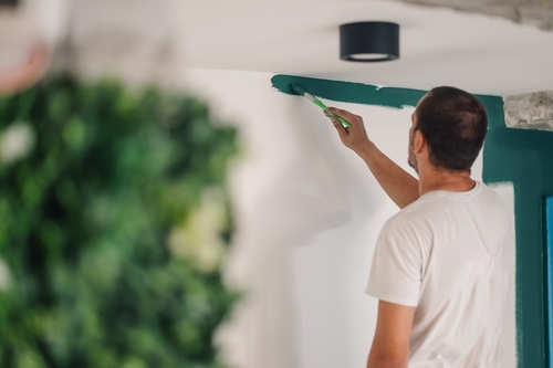 Professional house painter carefully applying green paint to a white wall, working on renovations in a modern apartment with stylish decor