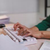 A person's hands are actively typing on a modern white keyboard while working at a desk
