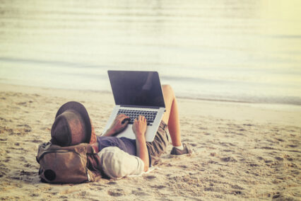 Young person using laptop on a beach.