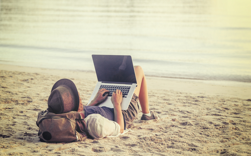 Young person using laptop on a beach.