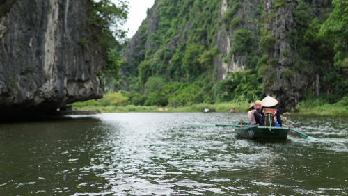 Tourists traveling in boat along the Ngo Dong River taking picture of the Tam Coc, Ninh Binh, Vietnam.