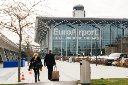 Commuters couple walking toward EuroAirport Basel Mulhouse Freiburg glass facade