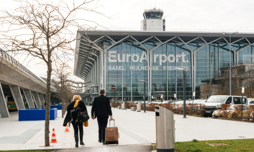 Commuters couple walking toward EuroAirport Basel Mulhouse Freiburg glass facade