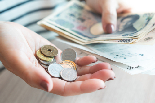 Closeup of a hand holding wads of Japanese banknote with sale slips from the convenience store and small coins in the other hand.