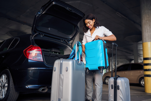 Happy woman with many suitcases in car parking