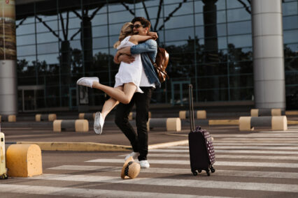 Happy brunette man hugs his girlfriend in white dress.