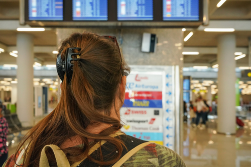 young woman at airport looking to departure tables, blurred airlines logos in background