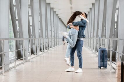 A man lifting up his girlfriend in air while standing together in an airport terminal hallway