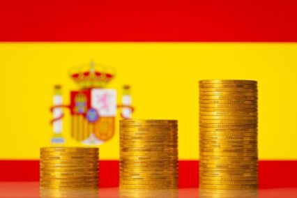 Up going graph made of coins stacked in front of Spain flag.