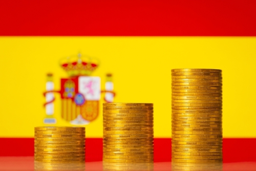 Up going graph made of coins stacked in front of Spain flag.