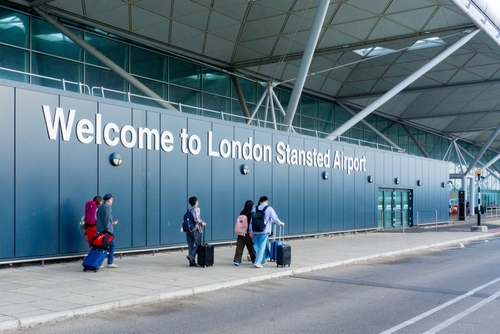 Welcome to London Stansted Airport sign with a group of travellers walking towards departures.